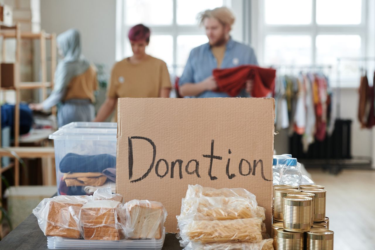 about-02 Volunteers sort clothes and food in a donation center. Cardboard sign reads 'Donation.'