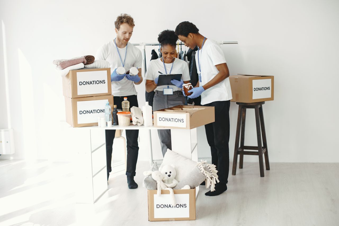 Three volunteers organize donation boxes filled with essentials in a bright indoor setting.