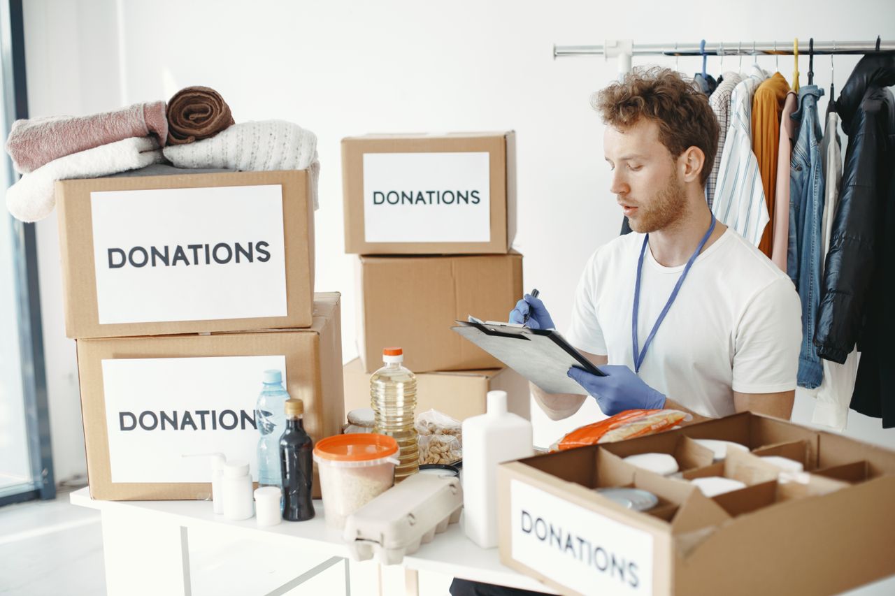 hero-about A man organizing donation boxes filled with clothes and food items at an NGO office.