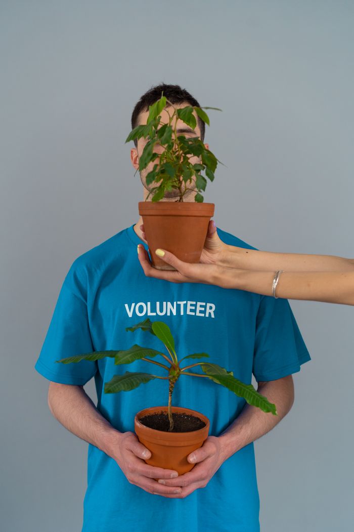 A volunteer holding potted plants symbolizes growth and environmental care indoors.